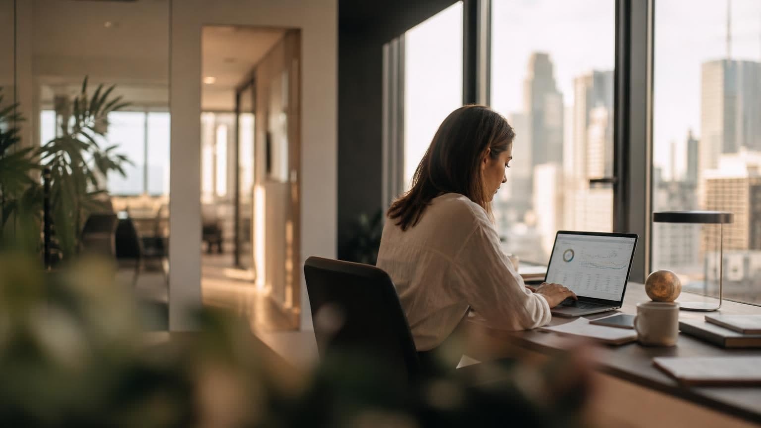 Marketing specialist werkt aan zoekmachine‑analyse op laptop, met stadssilhouet zichtbaar achter een groot raam.